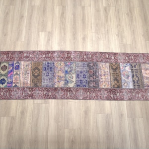 Può includere: Un tappeto lungo e stretto con un design a patchwork. Il tappeto è composto da tessuti di diversi colori con vari motivi, tra cui floreali, geometrici e paisley. Il tappeto ha un bordo bordeaux e un aspetto sbiadito e vintage.