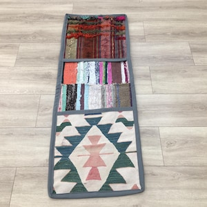 May include: A long, rectangular rug with a patchwork design. The rug is made of different fabrics and colors, including red, blue, green, and white. The rug is divided into three sections, each with a different pattern. The bottom section features a geometric pattern with a diamond shape in the center. The rug is perfect for adding a touch of bohemian style to any room.