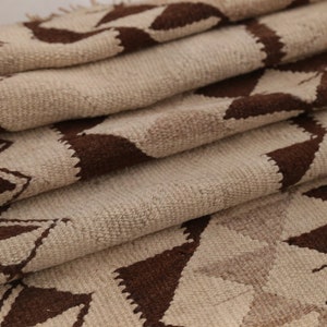 May include: A folded beige and brown woven rug with a geometric pattern. The rug is made of natural fibers and has a rustic, hand-woven look.
