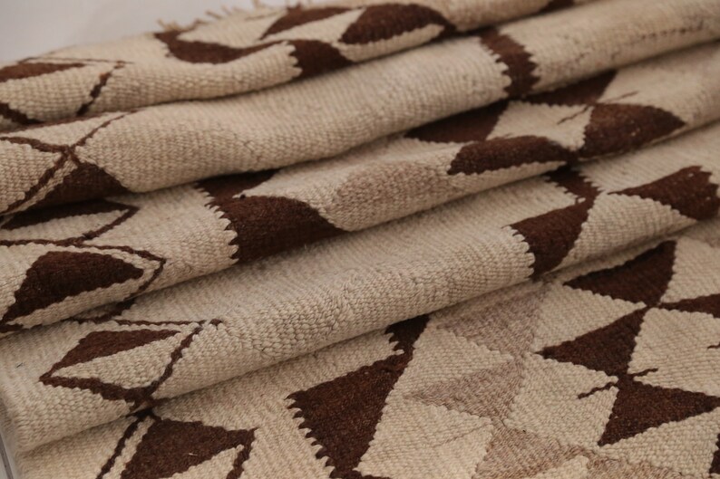 May include: A folded beige and brown woven rug with a geometric pattern. The rug is made of natural fibers and has a rustic, hand-woven look.