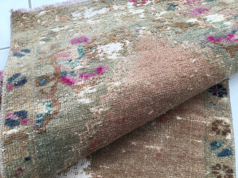 May include: A vintage rug with a faded floral pattern in shades of pink, blue, and green. The rug has a worn and distressed look, giving it a rustic charm.