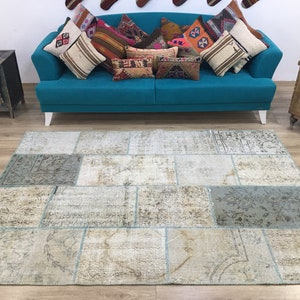 Könnte beinhalten: Ein hellblauer Patchwork-Teppich mit einem abgenutzten, Vintage-Look. Der Teppich besteht aus mehreren verschiedenen Stoffquadraten, die jeweils ein einzigartiges Muster aufweisen. Der Teppich liegt auf einem Holzboden vor einem türkisfarbenen Sofa mit Kissen.