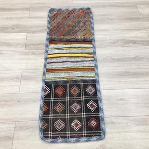 Puede incluir: Una alfombra larga y rectangular con un diseño de patchwork. La alfombra está hecha de diferentes telas y colores, incluyendo negro, blanco, rojo, amarillo y azul. La alfombra tiene un borde de flecos.