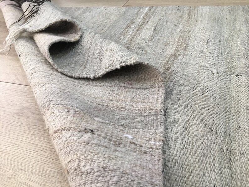 May include: A close-up of a light gray woven rug with a subtle striped pattern. The rug is rolled up and the texture of the weave is visible.