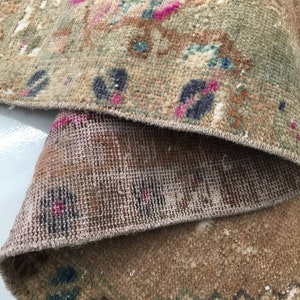 May include: Close-up of the back side of a rug with a woven pattern. The rug is a light brown color with a fringe border.
