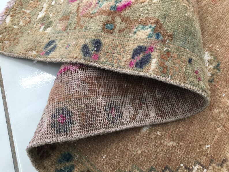 May include: Close-up of the back side of a rug with a woven pattern. The rug is a light brown color with a fringe border.