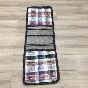 Puede incluir: Una alfombra rectangular con un diseño de patchwork. La alfombra está hecha de tres telas diferentes, cada una con un patrón diferente. La sección superior es un patrón de cuadros en tonos de rosa, blanco y negro. La sección media es una tela gris con rayas negras. La sección inferior es un patrón de cuadros en tonos de blanco, negro y rojo.
