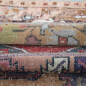 Könnte beinhalten: Nahaufnahme von gerollten Vintage-Teppichen mit komplizierten Mustern. Die Teppiche weisen eine Mischung aus Farben wie Beige, Rot, Blau und Grün auf. Die detaillierten Designs zeigen traditionelle Motive und erzeugen ein strukturiertes und geschichtetes Aussehen.