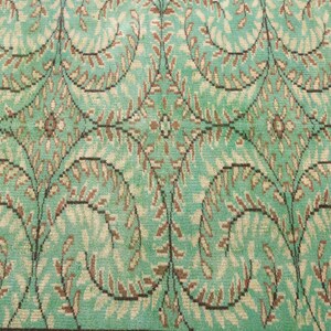 May include: A vintage rug with a repeating pattern of brown and green leaves on a light blue background.