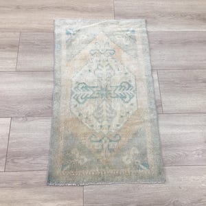 May include: A rectangular area rug featuring a central diamond medallion pattern in muted shades of sage green, beige, and cream. The design includes intricate floral and geometric motifs throughout the field, framed by a simple, narrow border.