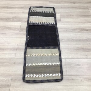 May include: A long, rectangular rug with a black center section and a striped pattern in shades of gray and white. The rug has a black border.