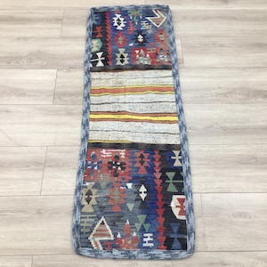 Puede incluir: Una alfombra larga y estrecha con un patrón geométrico azul, rojo y blanco. La alfombra tiene un borde de flecos y está hecha de tejido tejido.