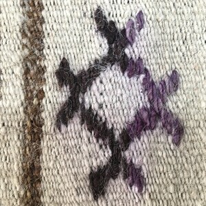 May include: Close-up of a woven rug with a geometric pattern in shades of brown, white, and purple.