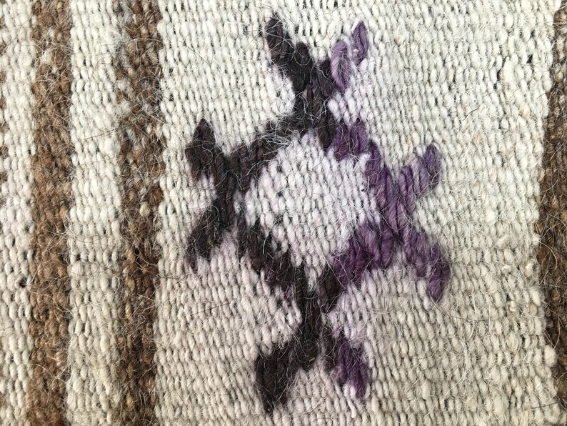 May include: Close-up of a woven rug with a geometric pattern in shades of brown, white, and purple.