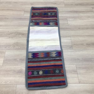 May include: A long, narrow, gray and white fabric storage organizer with three pockets. The pockets are decorated with colorful, geometric patterns.