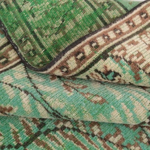 May include: Close-up of a folded green and brown patterned rug with a fringe border. The rug has a vintage look and feel.