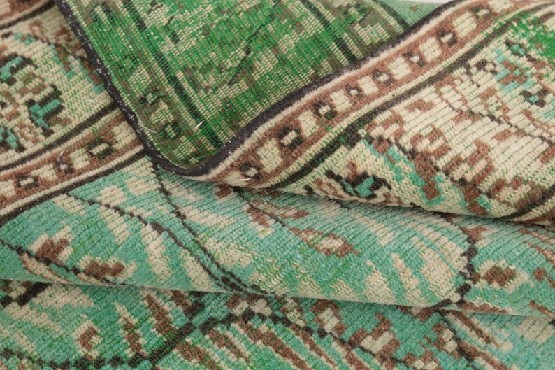 May include: Close-up of a folded green and brown patterned rug with a fringe border. The rug has a vintage look and feel.