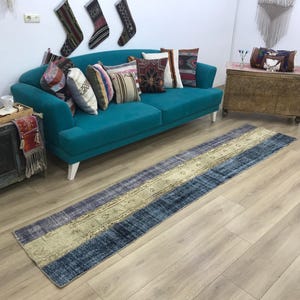 May include: A long, rectangular runner rug featuring a distressed, vintage-inspired pattern with a central beige band flanked by deep blue and grey sections. The rug displays intricate, faded floral and geometric motifs throughout its surface.