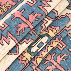 K&ouml;nnte beinhalten: Nahaufnahme eines gefalteten Teppichs mit einem geometrischen Muster in den Farben Rosa, Blau und Gelb.