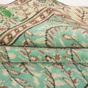 May include: A close-up of a folded turquoise and brown patterned rug with a geometric design.