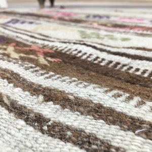 May include: Close-up of a woven rug with brown and white stripes. The rug has a textured surface and a subtle pattern.