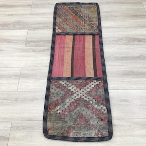 Puede incluir: Una alfombra larga y rectangular con un diseño de patchwork. La alfombra está hecha de telas de diferentes colores y tiene un borde azul oscuro. La alfombra está compuesta por tres secciones: una sección superior con un patrón geométrico, una sección central con rayas horizontales y una sección inferior con un patrón floral.