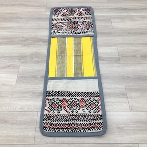 May include: A long, narrow, gray and white runner rug with a yellow and green striped section in the middle. The rug has a geometric pattern with red, black, and white accents.