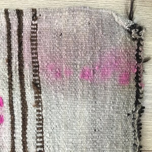 May include: Close-up of a woven rug with a brown and white striped pattern and pink accents. The rug has a frayed edge.