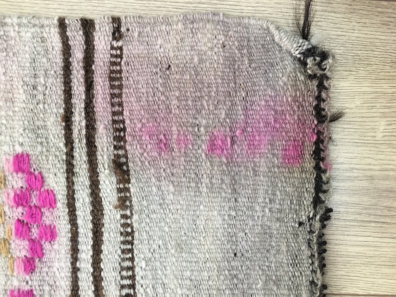 May include: Close-up of a woven rug with a brown and white striped pattern and pink accents. The rug has a frayed edge.