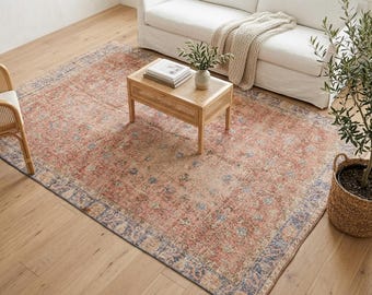 Könnte beinhalten: Ein großer rechteckiger Teppich mit einem verblassten, abgenutzten Muster in Terrakotta-, gedämpften Blau- und Cremetönen. Der Teppich hat eine markante Bordüre mit komplexen Blumenmotiven und ein Mittelfeld mit sich wiederholenden Medaillons.