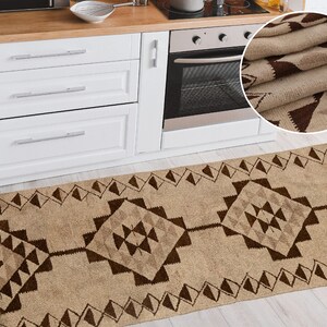 May include: A brown and beige patterned kitchen runner rug with a geometric design. The rug is placed in front of a white kitchen cabinet and a stainless steel oven.