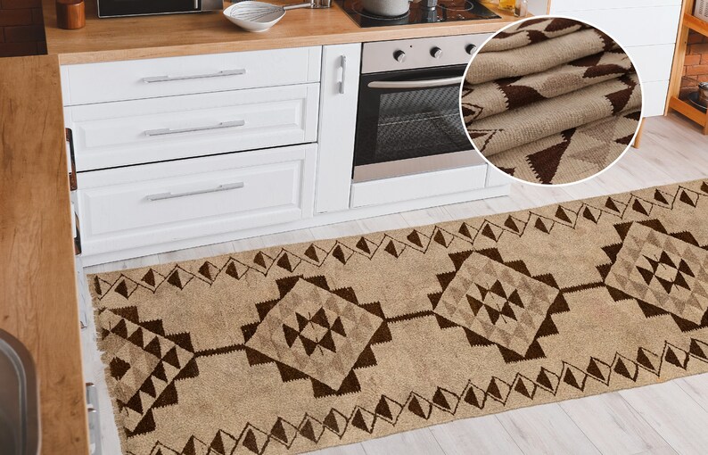 May include: A brown and beige patterned kitchen runner rug with a geometric design. The rug is placed in front of a white kitchen cabinet and a stainless steel oven.