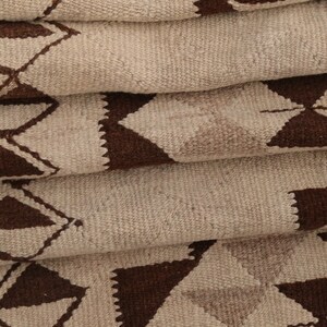 May include: A folded rug with a geometric pattern of brown triangles on a beige background.