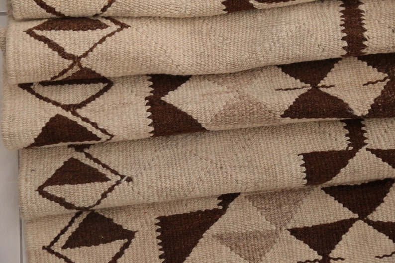 May include: A folded rug with a geometric pattern of brown triangles on a beige background.