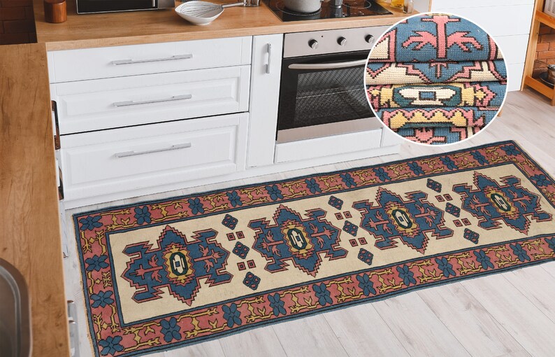 K&ouml;nnte beinhalten: Ein beige-blauer K&uuml;chenl&auml;ufer mit rotem Rand. Der L&auml;ufer hat ein traditionelles Design mit geometrischen Formen und floralen Motiven. Der L&auml;ufer ist in der oberen rechten Ecke des Bildes gefaltet, wodurch das Detail des Musters sichtbar wird.