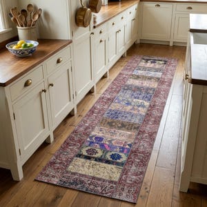 May include: A long rectangular runner rug featuring a patchwork design with various intricate patterns in shades of deep red, blue, brown, and cream. The rug has a wide, ornate border in a dark reddish-maroon tone with a repeating floral motif.