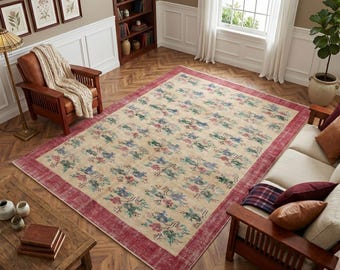 May include: A large rectangular area rug featuring a cream-colored field with a repeating floral pattern in shades of blue, green, and pink. The rug is framed by a wide, solid deep red border that contrasts with the lighter central design.