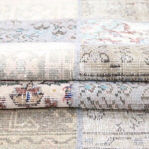 Pode incluir: Um tapete de patchwork composto por segmentos retangulares costurados. O tecido exibe uma variedade de padrões desbotados em tons suaves de bege, cinza, azul claro e creme, com pequenos detalhes em vermelho e azul escuro por toda a peça.