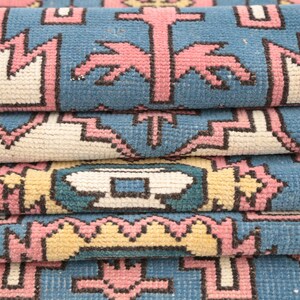 K&ouml;nnte beinhalten: Nahaufnahme eines gefalteten Teppichs mit einem geometrischen Muster in Rosa-, Blau- und Wei&szlig;t&ouml;nen.