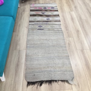 May include: A long, narrow, off-white rug with a fringe on the bottom. The rug has a woven pattern with colorful stripes and geometric designs.