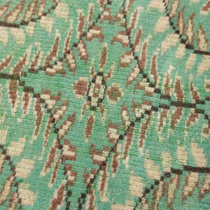 May include: Close-up of a green, brown, and white patterned rug. The rug has a woven texture and a geometric design.