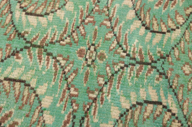 May include: Close-up of a green, brown, and white patterned rug. The rug has a woven texture and a geometric design.