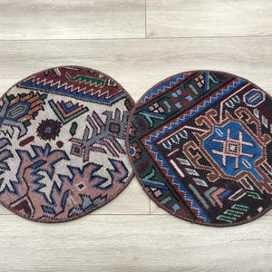 Puede incluir: Dos alfombrillas circulares tejidas con intrincados patrones geométricos en tonos azul, rojo, verde y crema. La alfombrilla izquierda tiene una base crema clara, mientras que la derecha tiene una base marrón oscura, ambas con bordes cosidos.