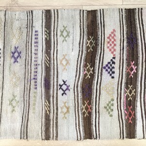 May include: A white, brown, and multi-colored woven rug with geometric patterns. The rug has a distressed look and is made of natural fibers.