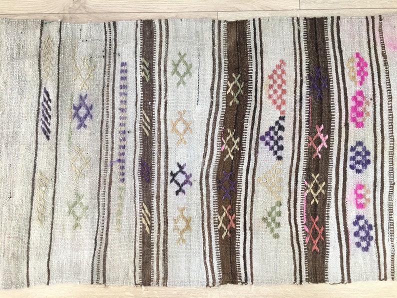 May include: A white, brown, and multi-colored woven rug with geometric patterns. The rug has a distressed look and is made of natural fibers.
