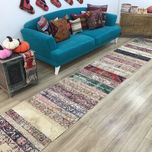 May include: A long, rectangular runner rug featuring a patchwork design composed of various vintage-style textile segments in shades of red, green, blue, cream, and brown, displaying intricate floral and geometric patterns throughout the surface.