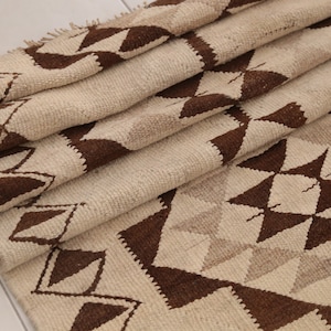 May include: A white and brown geometric patterned rug with a woven texture. The rug is folded in thirds, showing the pattern on the top and bottom layers.