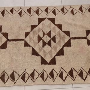 May include: A white and brown geometric patterned rug with a diamond pattern. The rug has a fringe border.