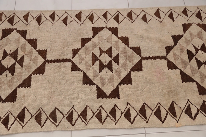 May include: A white and brown geometric patterned rug with a diamond pattern. The rug has a fringe border.