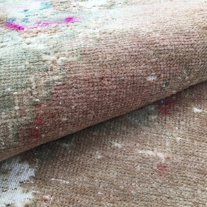 May include: Close-up of a beige and brown rug with a faded pink and blue pattern. The rug is rolled up, showing the texture of the fabric.